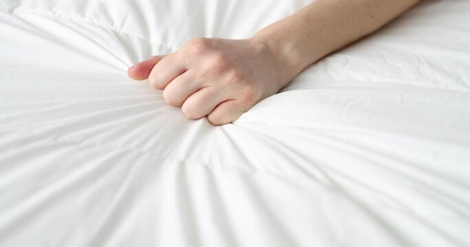 Woman hand tightly squeezes sheet on bed