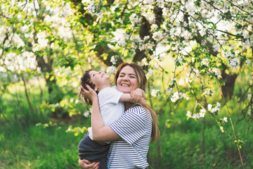 Fototapeta premium Mother with little baby son in spring garden during golden hour. Mom and son are active in nature. Family walks in a spring garden. Happy mother's day