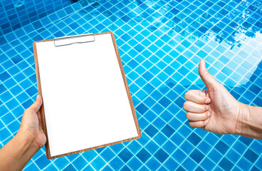Blank paper on wooden clipboard with girl hand over crystal clear swimming pool water, water...