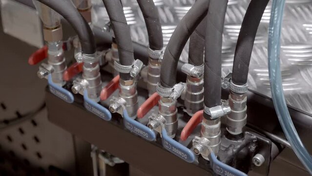Many reinforced hoses enter the hydraulic unit of the equipment and through ball valves, the volume of liquid is regulated. Closeup. Shot in motion
