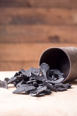 coconut shell charcoal scattered on table top from a container, carbonized raw shells in a limited...