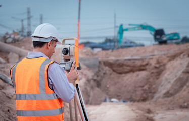 Surveyor engineer wearing safety uniform ,helmet and radio communication with equipment theodolite to measurement positioning on the construction site of the road with construct machinery background