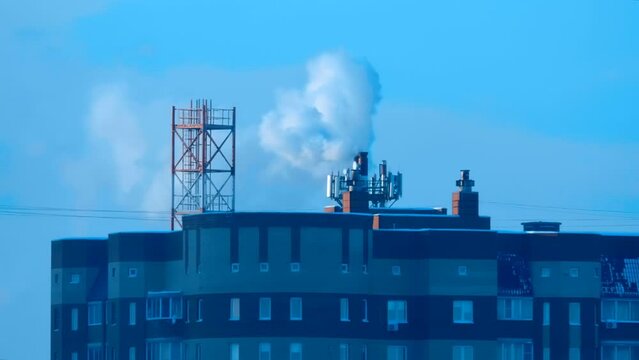 Puffs of steam from a pipe of a gas boiler house that heats a microdistrict of brick high-rise buildings in a cold winter