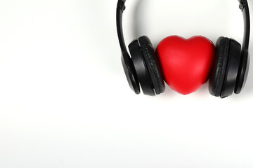 Black headphones with red heart sign in the middle on white surface. Concept for music festivals,...