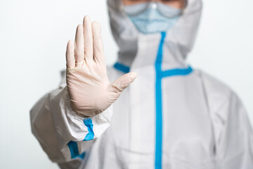 Doctor or nurse wearing protective suit and mask showing stop gesture on the white background.