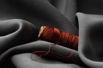 Reel with brown threads on gray silk fabric, macro, texture, close-up. Luxurious bright beautiful background for sewing. Tailoring, the concept of the atelier. High fashion, natural fabrics
