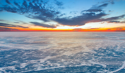A granite rock with steep slopes rises above a frozen lake with reflection on the ice at sunset -  Lake Baikal, Russia