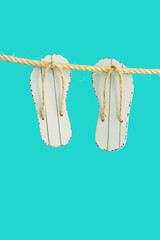 Summer concept, grey toy flip-flops hanging on rope. Bright summer minimal style.