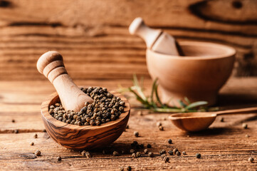 Black pepper in wood bowl on wooden table. Spices on desk. Organic spice dry peppercorn.