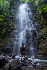 tourist man looking at a waterfall surrounded by vegetation in the middle of the humid tropical jungle of Costa Rica