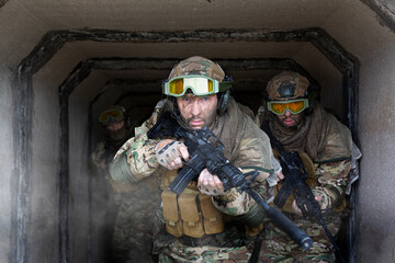 Three military mercenaries walk against the background of a concrete wall and smoke. Photo with...