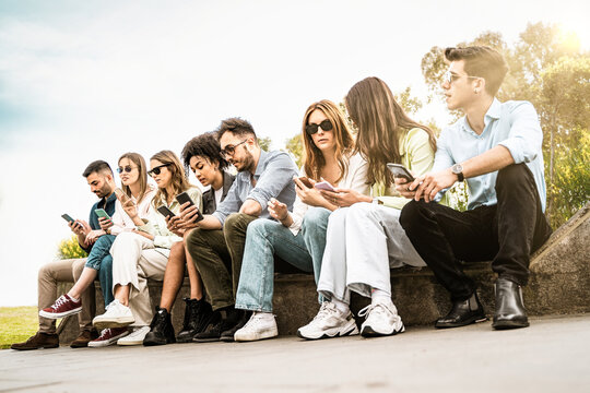 Youth friends community phubbing using smartphones sitting outdoors on a bench - lifestyle people and technology concept - filtered image - low angle view