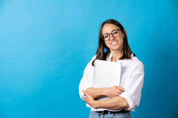 Pretty hispanic woman holding laptop and looking at camera isolated on blue background. Happy...