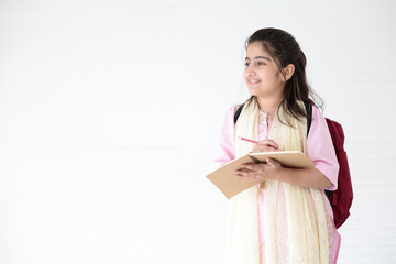 Obraz premium cute Indian girl smiling and writing on notebook for learning, education concept