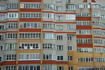 Многоэтажный жилой дом из серого кирпича с оранжевыми и красными лоджиями и балконами.