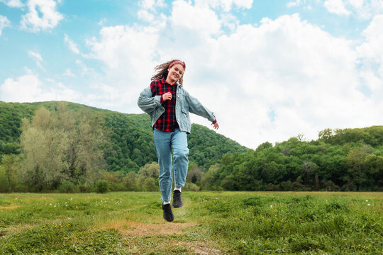 A happy teen girl is skipping across the field. Mountains and sky are in the background. The concept of freedom and psychology