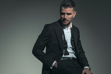 sexy elegant man in tuxedo looking away and posing with hand in pocket