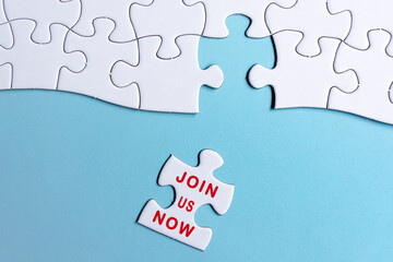 White jigsaw puzzle with word join us now over blue background.