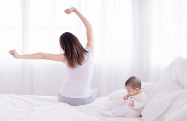 Beautiful Asian mother and daughter waking up in the morning. Young women stretching arms up in the bedroom at home. mom and infant waking up after sleeping in bed together.