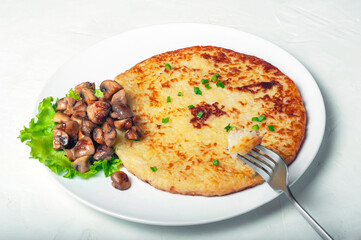 A traditional Swiss dish is a potato pancake on a white plate with fried mushrooms and a leaf of green salad. on a potato tortilla there is a fork with a piece of fried potatoes on it.