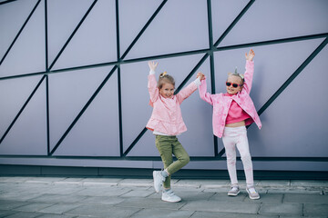 Two little girls wearing stylish pink clothes, having fun outdoors.