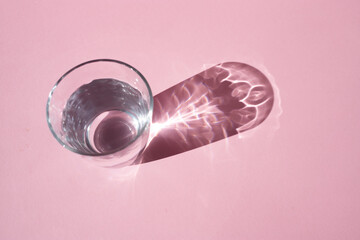 A glass glass with water casts a shadow on a pink background.