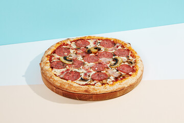 Italian pizza with salami, bacon and mushroom on coloured background. Meat pizza with salami and bacon in minimal style on blue and orange color. American pizza delivery concept with color backdrop