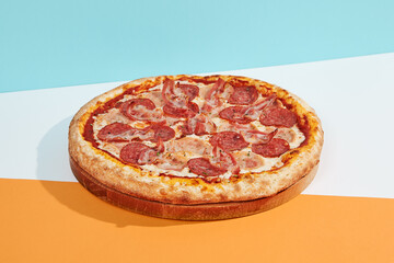 talian pizza with salami, ham, bacon, pepperoni on coloured background. Meat pizza with sausage and bacon in minimal style on blue, orange color. American pizza delivery concept with color backdrop.