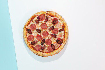 Italian pizza with chicken, salami and sausage on coloured background. Meat pizza with chicken and salami in minimal style on blue color. American pizza delivery concept with color backdrop.