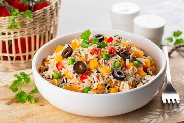 Healthy dinner with Rice Salad with fresh vegetables, bell bebber, tomato, green pea, black olives and olive oil,  on a white table.