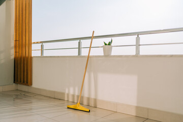 Broom standing on the balcony tiled floor in the summer day. Cleaning equipment with flower pot on...