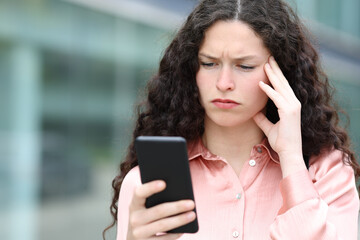 Worried woman reading message on phone in the street