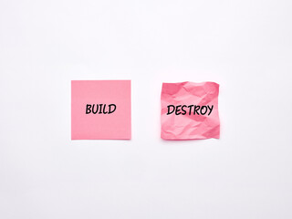 The words build and destroy on pink sheets of note paper.