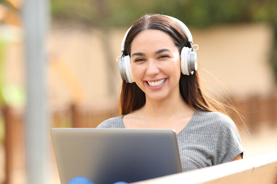 Happy woman with headphones and laptop looks at you