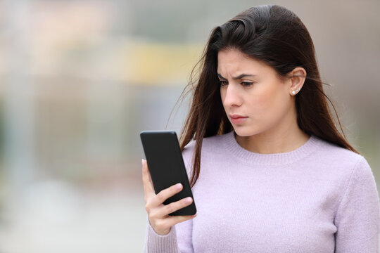 Worried woman reads phone content in the street