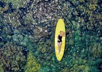 High angle view of an asian girl with black hair lying on a surfboard in the middle of the sea, hat...