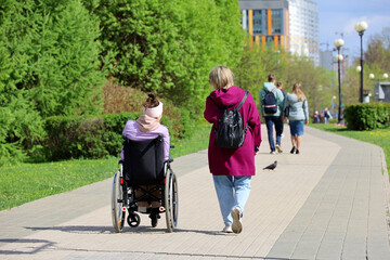 Disabled person in a wheelchair and woman walking on a city street. Care for handicapped people