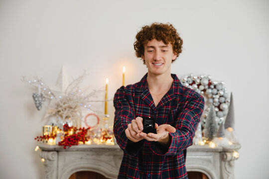 Smiling man showing engagement ring in front of marble fireplace at home