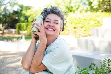 Happy woman with bottles of smoothie sitting in garden