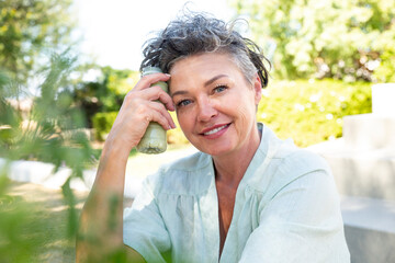 Smiling woman with bottle of smoothie sitting in garden