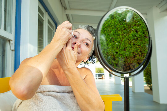 Smiling Mature Woman Putting Drops In Eye Looking At Mirror