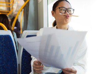 Businesswoman with pencil on puckering lips sitting with documents in tram