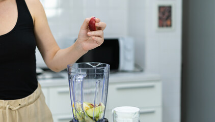 apple in hand of vegetarian woman mixing fruit juice in kitchen with copy space. beautiful caucasian woman cooking healthy diet fruit or vegetable in kitchen