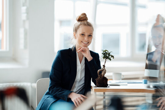 Smiling businesswoman sitting with plant on desk at office