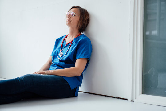 Tired female doctor leaning on wall relaxing at hospital corridor