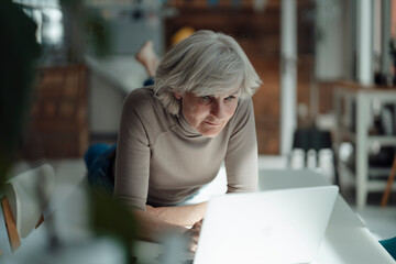 Senior woman using laptop lying on desk in office