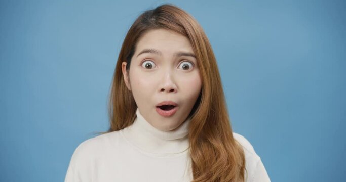 Close-up attractive youth Asia Lady with sweater excited surprised and amazed opened mouth raise eyebrows, shocked woman can't believe her eyes, look at camera isolated on the blue background.