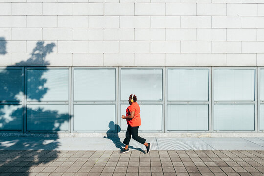 Woman listening music through wireless headphones jogging on footpath - Powered by Adobe