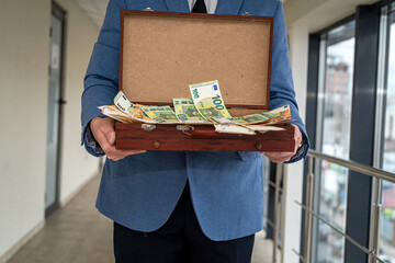 a man in suit stands with an open case in which a large amount of money for the arrangement.