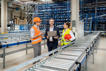 Blue-collar workers discussing over laptop with businessman in warehouse